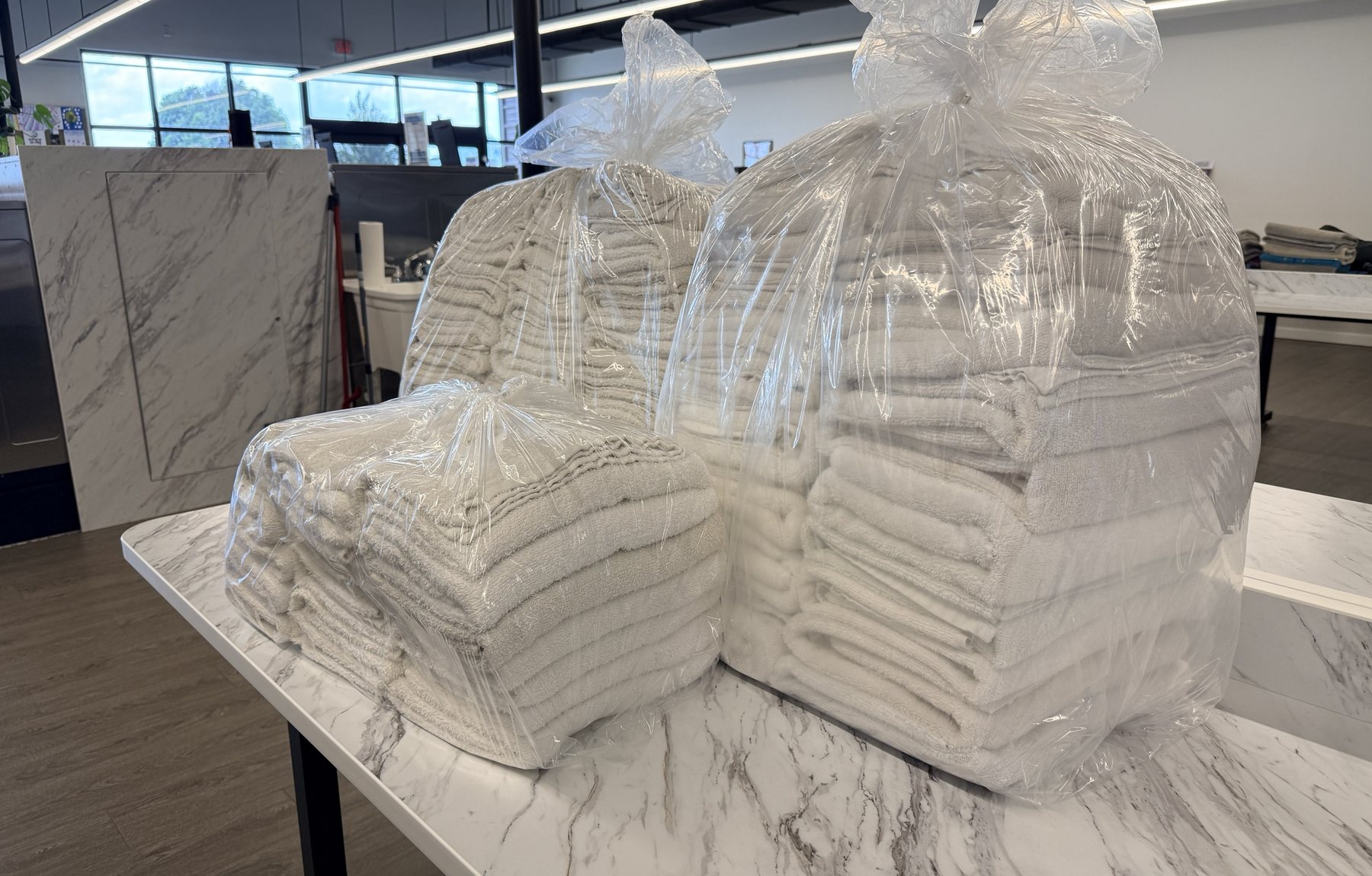 Bags of clean, folded white towels on the marble counter at Top Tier Coin Laundry
